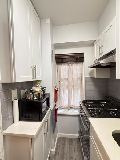 Kitchen with backsplash, black range oven, white cabinets, and light stone countertops