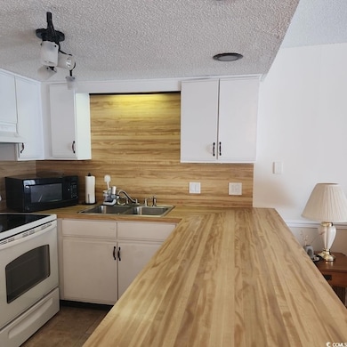 Kitchen featuring butcher block countertops, white electric range, black microwave, a textured ceiling, and white cabinets