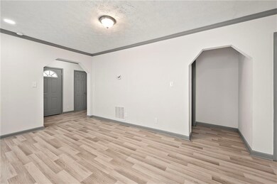 Spare room with arched walkways, light wood-style flooring, a textured ceiling, baseboards, and crown molding