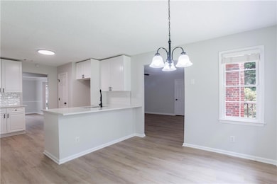 Kitchen with light wood finished floors, a chandelier, white cabinets, and a textured ceiling