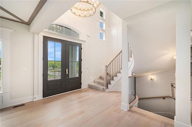 Foyer with wood finished floors, french doors, a chandelier, a towering ceiling, and stairway