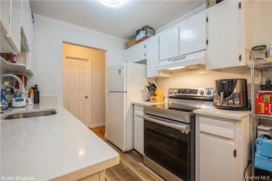 Kitchen featuring exhaust hood, light hardwood flooring, white refrigerator, white cabinets, and stainless steel electric range oven
