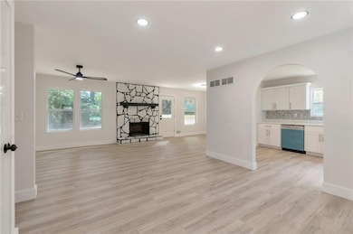 Unfurnished living room featuring arched walkways, a stone fireplace, ceiling fan, plenty of natural light, and recessed lighting
