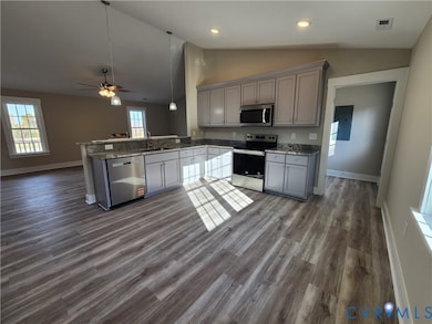 Kitchen featuring open floor plan, gray cabinets, stainless steel appliances, hanging light fixtures, and a peninsula