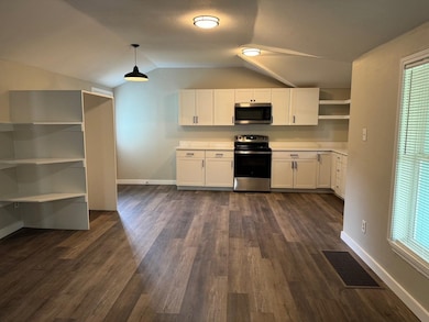 Kitchen featuring open shelves, white cabinets, appliances with stainless steel finishes, light countertops, and vaulted ceiling
