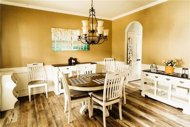 Dining room with arched walkways, wood finished floors, ornamental molding, a chandelier, and a wainscoted wall