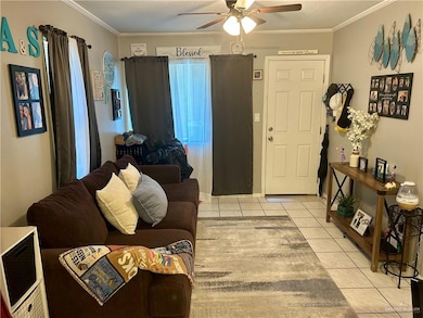 Living area with light tile patterned floors, crown molding, and ceiling fan