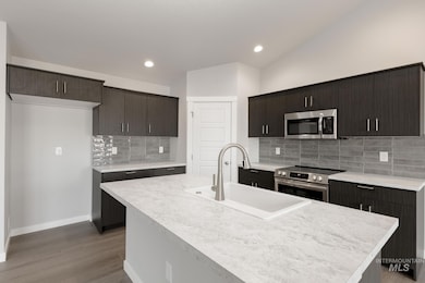 Kitchen with light countertops, appliances with stainless steel finishes, dark brown cabinets, a kitchen island with sink, and recessed lighting