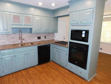 Kitchen with black appliances, blue cabinets, tasteful backsplash, wood finished floors, and recessed lighting