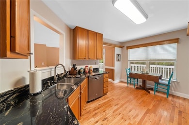 Kitchen with stainless steel dishwasher, brown cabinetry, light wood finished floors, and dark stone countertops