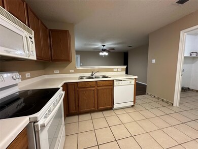 Kitchen with white appliances, a peninsula, ceiling fan, a sink, and a textured ceiling