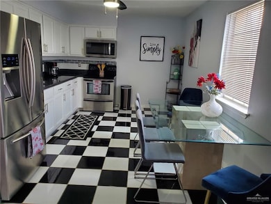 Kitchen featuring stainless steel appliances, tile patterned floors, white cabinetry, and backsplash