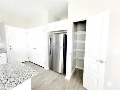Kitchen with baseboards, light stone countertops, light wood-type flooring, freestanding refrigerator, and white cabinetry