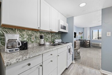 Kitchen with white appliances, a sink, white cabinetry, light wood-type flooring, and light stone counters