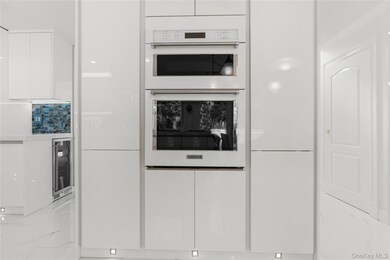 Kitchen with white cabinets, double oven, modern cabinets, beverage cooler, and light marble finish flooring