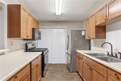 Stainless steel appliances, decorative backsplash, a textured ceiling, and light countertops