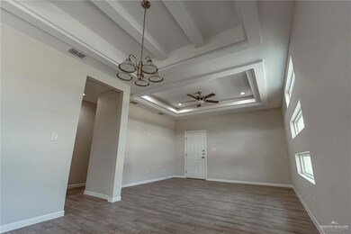 Spare room featuring wood-type flooring, ceiling fan with notable chandelier, beam ceiling, and a tray ceiling