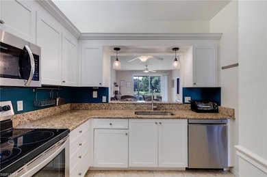 Kitchen with appliances with stainless steel finishes, white cabinets, light stone counters, and hanging light fixtures