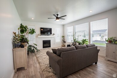 Living room with a glass covered fireplace, light wood-type flooring, a ceiling fan, and recessed lighting