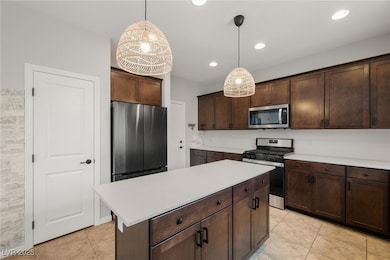 Kitchen featuring appliances with stainless steel finishes, dark brown cabinets, light countertops, pendant lighting, and a kitchen island