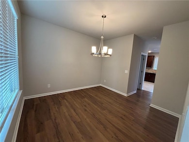 Empty room with dark wood-style flooring, a chandelier, and baseboards
