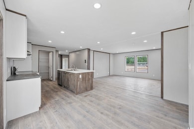 Kitchen with light wood-style floors, an island with sink, recessed lighting, open floor plan, and a sink