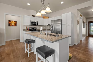 Kitchen featuring a kitchen bar, stainless steel appliances, decorative light fixtures, a kitchen island with sink, and white cabinetry