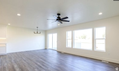Unfurnished living room with dark wood-type flooring, ceiling fan, a chandelier, and recessed lighting