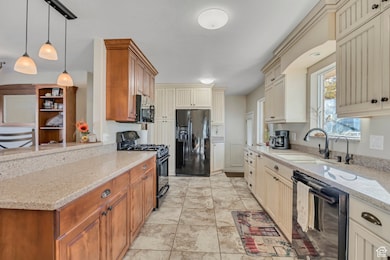 Kitchen featuring light stone counters, black appliances, pendant lighting, light tile patterned floors, and brown cabinetry