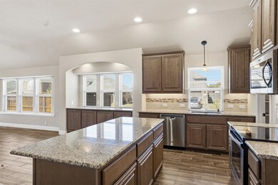 Kitchen with wood tiled floors, light stone countertops, decorative backsplash, decorative light fixtures, and stainless steel appliances