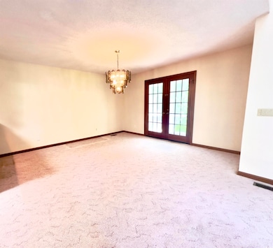 Unfurnished room featuring french doors, a chandelier, and light carpet