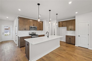 Kitchen featuring decorative backsplash, stainless steel appliances, hanging light fixtures, an island with sink, and dark wood-style floors