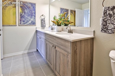 Bathroom with double vanity, tile patterned flooring, toilet, baseboards, and a textured wall