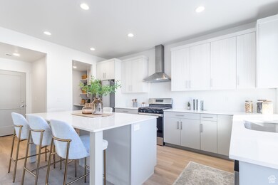 Kitchen with light wood-style flooring, stainless steel appliances, wall chimney exhaust hood, a center island, and a breakfast bar
