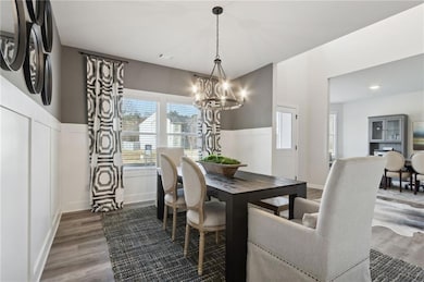 Dining area with a chandelier, a decorative wall, wood finished floors, and a wainscoted wall