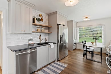 Kitchen featuring dark countertops, backsplash, appliances with stainless steel finishes, open shelves, and dark wood-type flooring