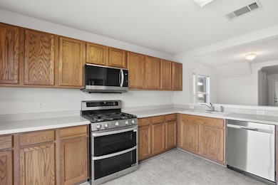 Kitchen with stainless steel appliances, brown cabinetry, and light countertops