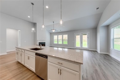 Kitchen featuring vaulted ceiling, white cabinetry, open floor plan, light stone countertops, and ceiling fan
