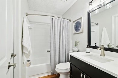 Full bathroom featuring hardwood / wood-style floors, shower / bath combination with curtain, a textured ceiling, toilet, and vanity