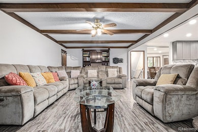 Living room with beamed ceiling, a textured ceiling, wood finished floors, and ceiling fan