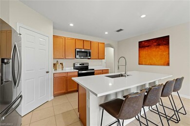 Kitchen featuring arched walkways, appliances with stainless steel finishes, recessed lighting, light tile patterned flooring, and a center island with sink