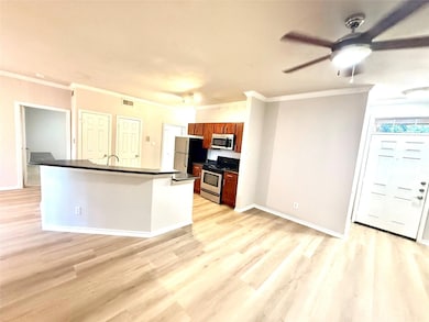 Kitchen with dark countertops, stainless steel appliances, light wood finished floors, brown cabinets, and ornamental molding