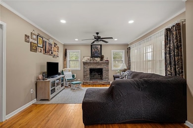 Living area featuring crown molding, hardwood floors, recessed lighting, a stone fireplace, and a ceiling fan