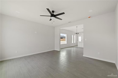 Unfurnished living room with a ceiling fan, dark wood-style floors, and a chandelier