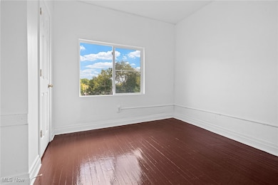 Spare room featuring dark wood-style floors and baseboards