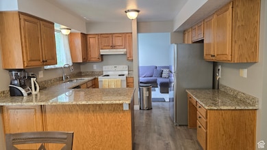 Kitchen featuring white range with electric cooktop, wood finished floors, a peninsula, freestanding refrigerator, and light stone counters