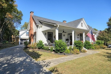 View of front of property featuring a chimney, a porch, a front lawn, a shingled roof, and a garage