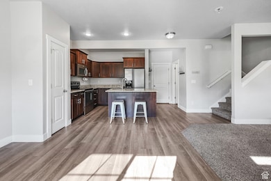 Kitchen with a kitchen breakfast bar, stainless steel appliances, light wood-style flooring, an island with sink, and dark brown cabinets