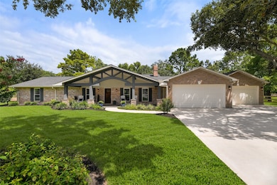 An extra-long paved driveway leads from Falling Leaf Drive amidst the towering trees that dot this property to this charming single-story home with ample parking space and a brick elevation with wood shutters and the most inviting gabled front porch.