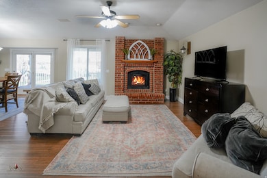 Living area with dark wood finished floors, a fireplace, a ceiling fan, and lofted ceiling
